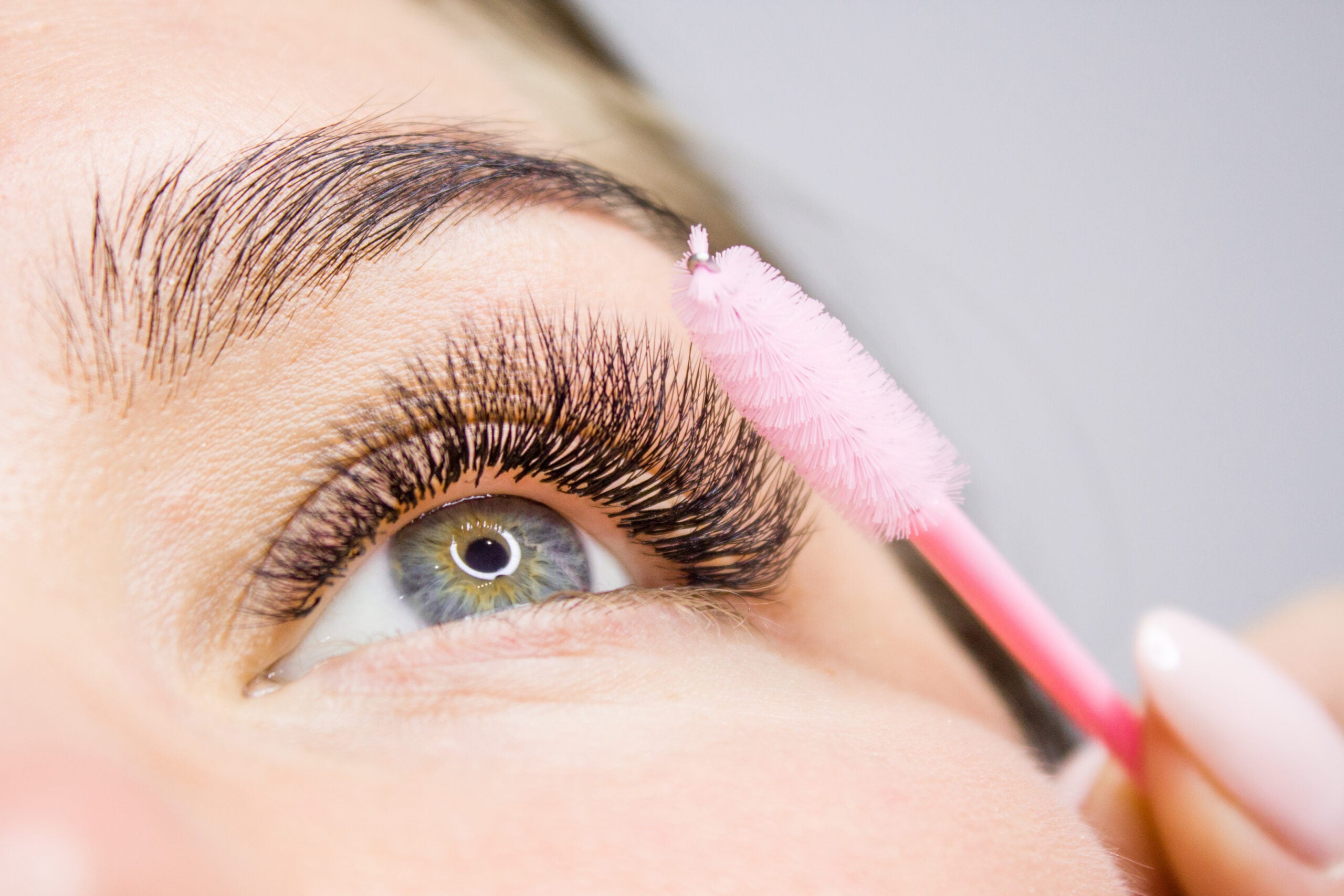 Eyelash Extension Procedure. Woman Eye with Long false Eyelashes. Close up macro shot of fashion eyes visagein in beauty salon. using brushes for DIY lash extensions